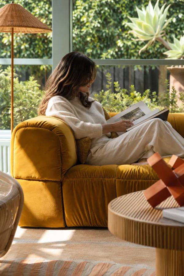 Mujer leyendo en un sofá de terciopelo mostaza